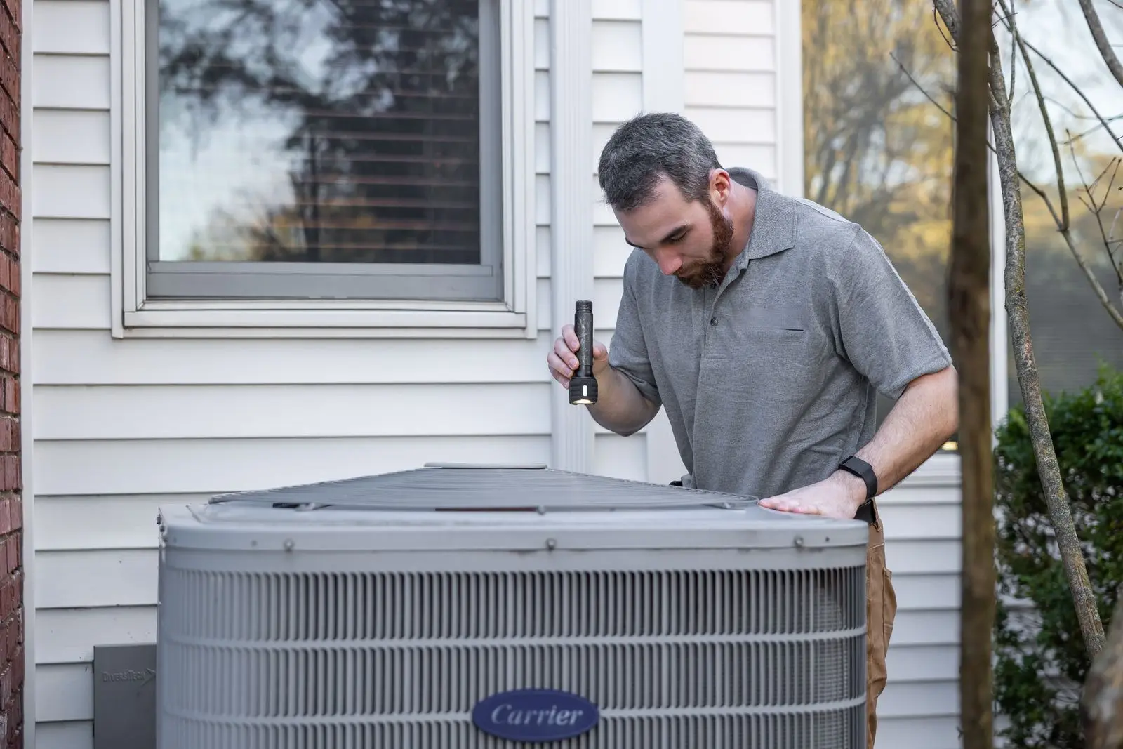 HVAC technician working on an outdoor AC condenser beside a house